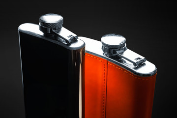 Two flask for alcohol. Steel flask with leather trim stand side by side on a black background....