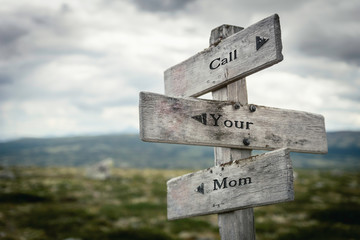 Call your mom text on wooden rustic signpost outdoors in nature/mountain scenery. Family and care concept.