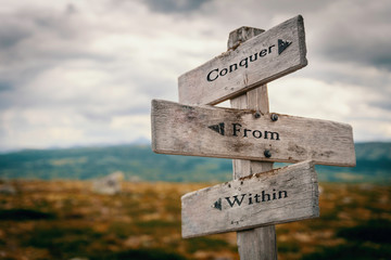 Conquer from within text on wooden rustic signpost outdoors in nature/mountain scenery.