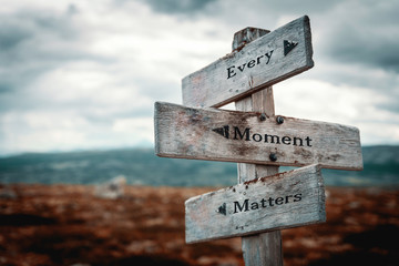 Every moment matters text on wooden rustic signpost outdoors in nature/mountain scenery. Time is...