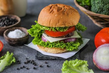 Photo of fresh burger on wooden cutting board on dark background..Homemade hamburger with beef, onion, tomato, lettuce and cheese. Homemade fast food. Dark textured background. Copy space. Image.