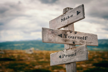 Make yourself proud text quote on wooden rustic signpost outdoors in nature/mountain scenery....