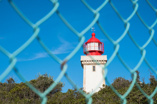 Alfanzina Lighthouse at southern coast of Portugal thrrough the fence, Algarve, Portugal