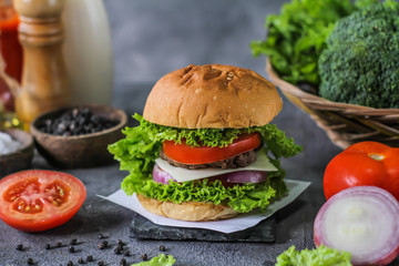Photo of fresh burger on wooden cutting board on dark background..Homemade hamburger with beef, onion, tomato, lettuce and cheese. Homemade fast food. Dark textured background. Copy space. Image.