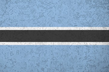 Botswana flag depicted in bright paint colors on old relief plastering wall. Textured banner on...
