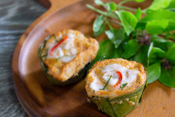 Steamed fish with curry paste in banana leaf cup and basil leaf in wooden tray thai food (Thai language call Hor mok) on wooden gray floor