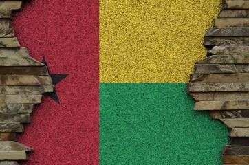 Guinea Bissau flag depicted in paint colors on old stone wall closeup. Textured banner on rock wall...