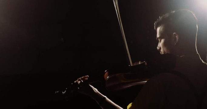 Silhouette of young guy popular musician playing solo on his instrument. Portrait of young man professional violinist playing violin on stage in spotlight. Classical music player palying on concert.