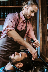 handsome barber with tattoo washing hair of bearded man with closed eyes