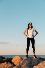 The concept of sport and a healthy lifestyle. A young woman in sportswear , standing on the coastal rocks, hands on hips. Copy space