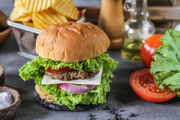 Photo of fresh burger on wooden cutting board on dark background..Homemade hamburger with beef, onion, tomato, lettuce and cheese. Homemade fast food. Dark textured background. Copy space. Image.