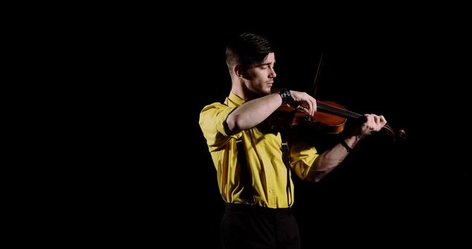 Guy musician playing solo on alt. Man professional violinist plays violin on black background in darkness, front view. Elegant person performs classical composition on fiddlestick instrument.