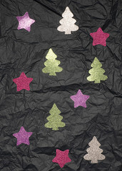 Shiny Christmas trees and stars on a dark crumpled background.