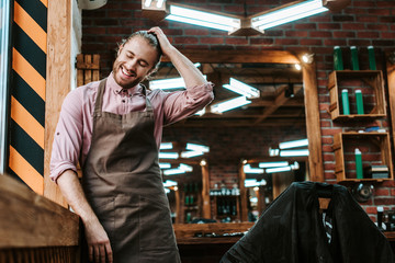 selective focus of happy barber in apron touching hair in barbershop