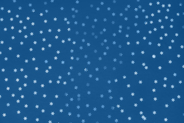 Metallic foil snowflakes confetti sparse on trendy classic blue colored background. Simple holiday concept. Winter festive backdrop. Top view, flat lay. Color of the year 2020