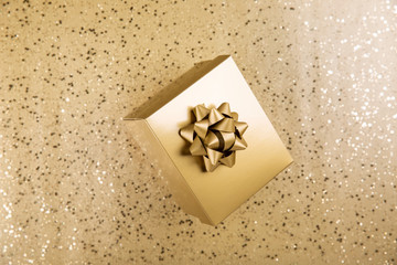 Golden gift box with gold bow on  shiny background. Top view, copy space.