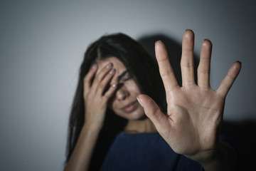 Crying young woman making stop gesture near white wall, focus on hand. Domestic violence concept