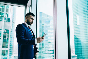 Pensive adult businessman using smartphone in office