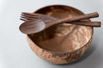 recycling, tableware and eco friendly concept - close up of coconut bowl with brown wooden spoon...