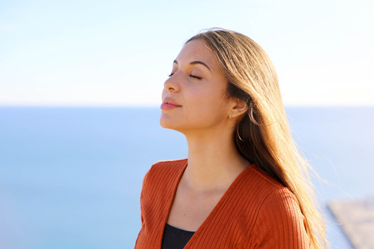 Close up of beautiful relaxed girl breathing fresh air with blue sea on the background.