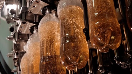 Production and bottling of beverages carbonated lemonade, soda or beer in plastic bottles on automatic conveyor on industrial plant. Food industry concept. Manufacturing of bottled drinks.