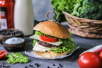 Photo of fresh burger on wooden cutting board on dark background..Homemade hamburger with beef, onion, tomato, lettuce and cheese. Homemade fast food. Dark textured background. Copy space. Image.
