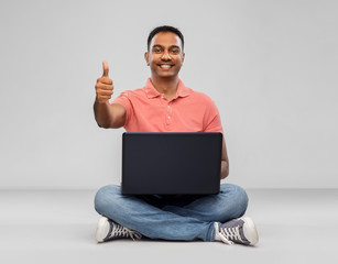 technology, internet, communication and people concept - happy indian man with laptop computer sitting on floor over grey background