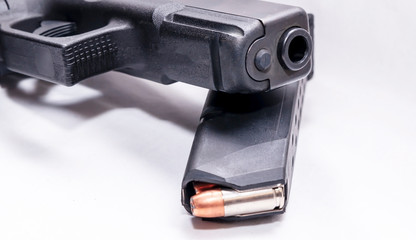 A black 9mm pistol on top of a pistol magazine loaded with hollow point bullets on a white background