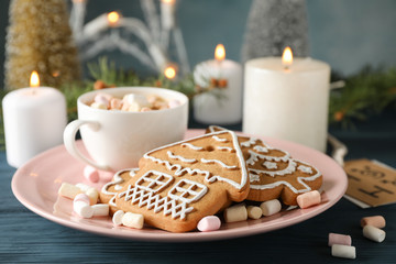 Plate of homemade Christmas cookies, coffee, marshmallows on wooden table, against blue background, space for text. Closeup