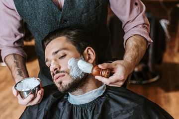 Barber applying shaving cream on face of handsome bearded man