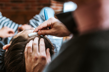 selective focus of barber holding razor while doing haircut to man