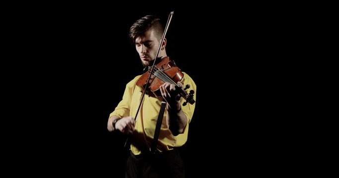 Man virtuoso violinist playing violin on black background in darkness, front view. Guy musician violist playing solo on alt. Elegant person performs classical composition on fiddlestick instrument.