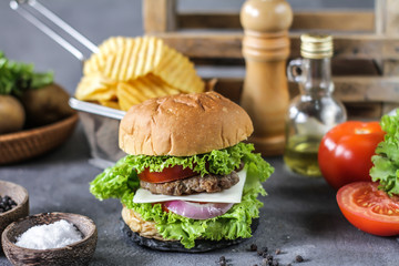 Photo of fresh burger on wooden cutting board on dark background..Homemade hamburger with beef, onion, tomato, lettuce and cheese. Homemade fast food. Dark textured background. Copy space. Image.