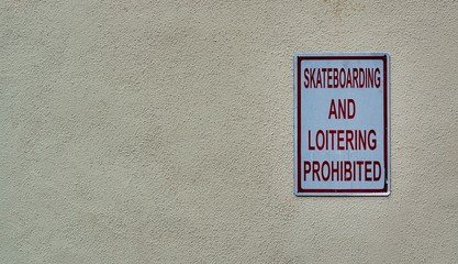 Skateboarding and Loitering Prohibited sign attached to a plain textured exterior wall. Placed to the right leaving copy space around it.