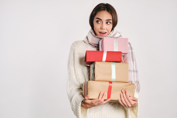 Pretty excited girl in sweater with scarf holding gift boxes surprisingly looking away over white background