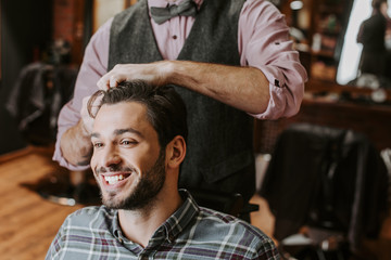 barber styling hair on cheerful bearded man
