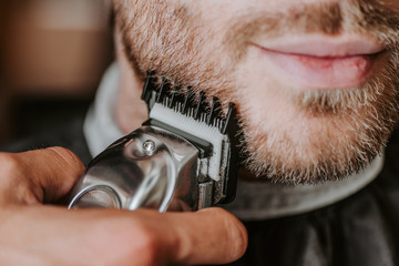 close up of barber holding trimmer while shaving man