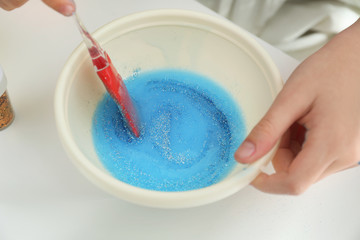 Little girl mixing ingredients with silicone spatula at table, closeup. DIY slime toy