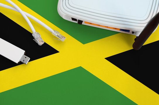 Jamaica flag depicted on table with internet rj45 cable, wireless usb wifi adapter and router. Internet connection concept