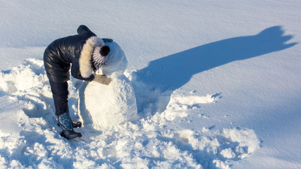 Girl sculpts a snowman in the snow