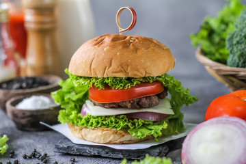 Photo of fresh burger on wooden cutting board on dark background..Homemade hamburger with beef, onion, tomato, lettuce and cheese. Homemade fast food. Dark textured background. Copy space. Image.
