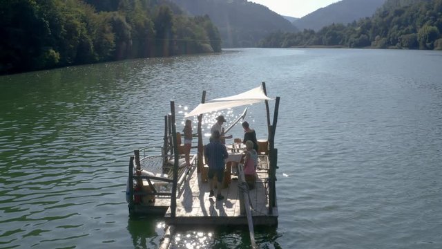 Family eating on river boat along shimmering blue water in muta, slovenia: angle one mid tele aerial