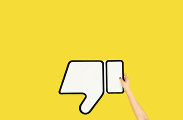 Hands holding the sign of dislike on yellow studio background. Negative space to insert your text...