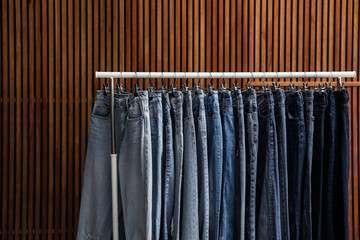Rack with different jeans on wooden background