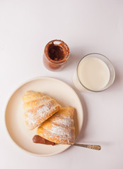 Fresh croissants bun with chocolate on the plate, glass of milk on the white background