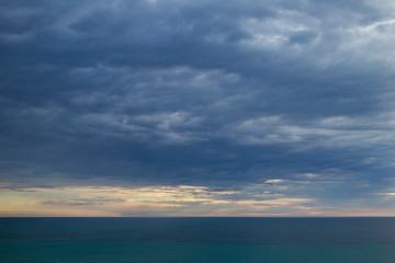 Dark dramatic cloudscape over blue sea water. Heavy clouds of thunderstorm. Horisontal color photography.