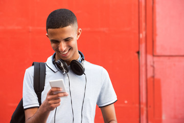 Close up smiling young arabic man looking at mobile phone by red background