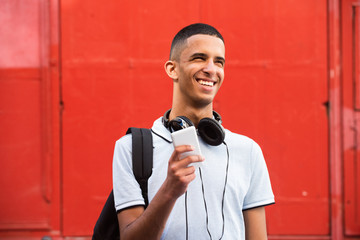 Close up smiling young arabic man with mobile phone and bag by red background