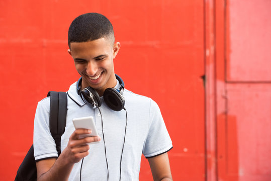 Close Up Smiling Young Arabic Man Looking At Mobile Phone By Red Background