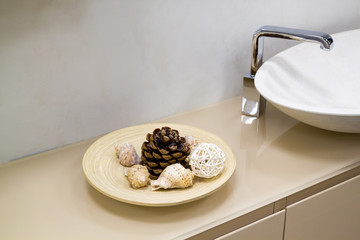 close up view of shelf in bathroom with decor in form of dish with cone and shells and white ceramic sink with chrome tap